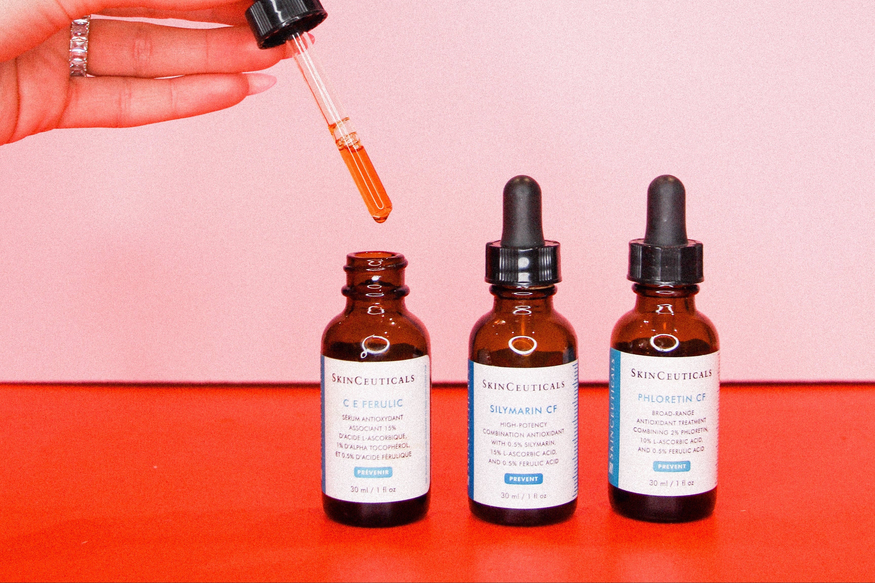 Three bottles of Skinceuticals on a red surface with a pink background